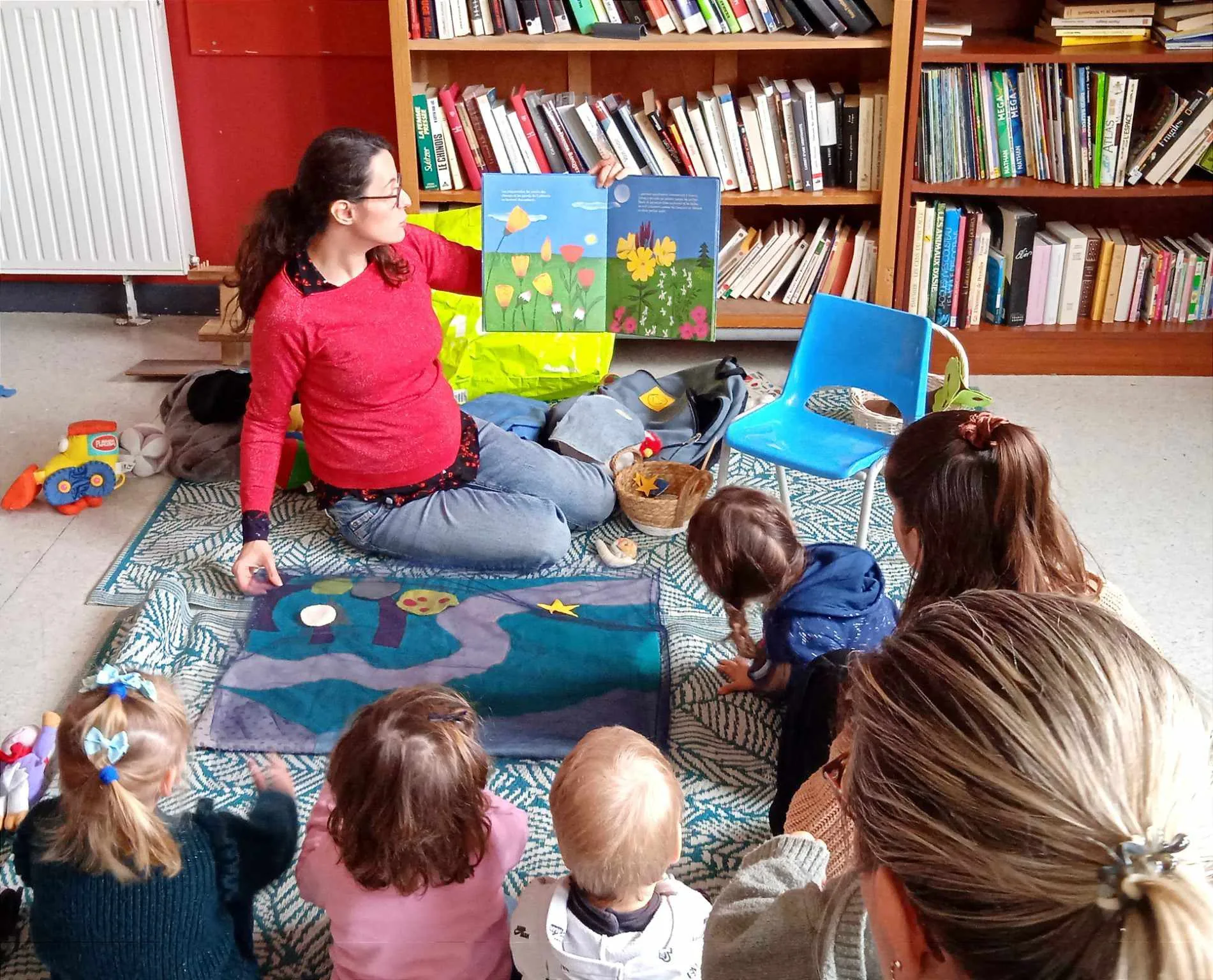 Racontée en médiathèque : Laetitia montre un album aux enfants assis devant le tapis de lecture