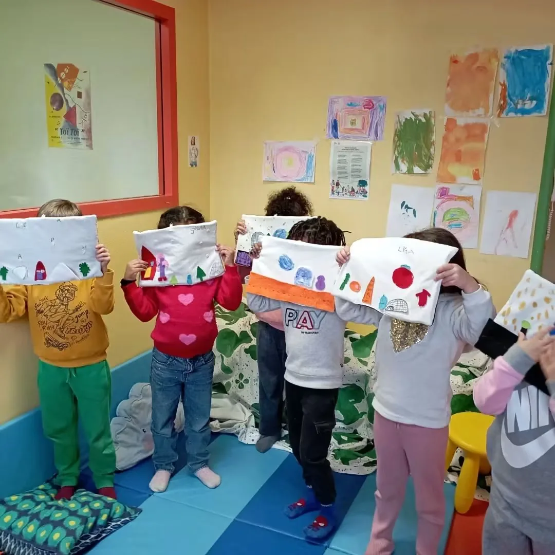 Des enfants brandissent les mini-tapis de lecture qu'ils viennent de fabriquer, cachés derrière