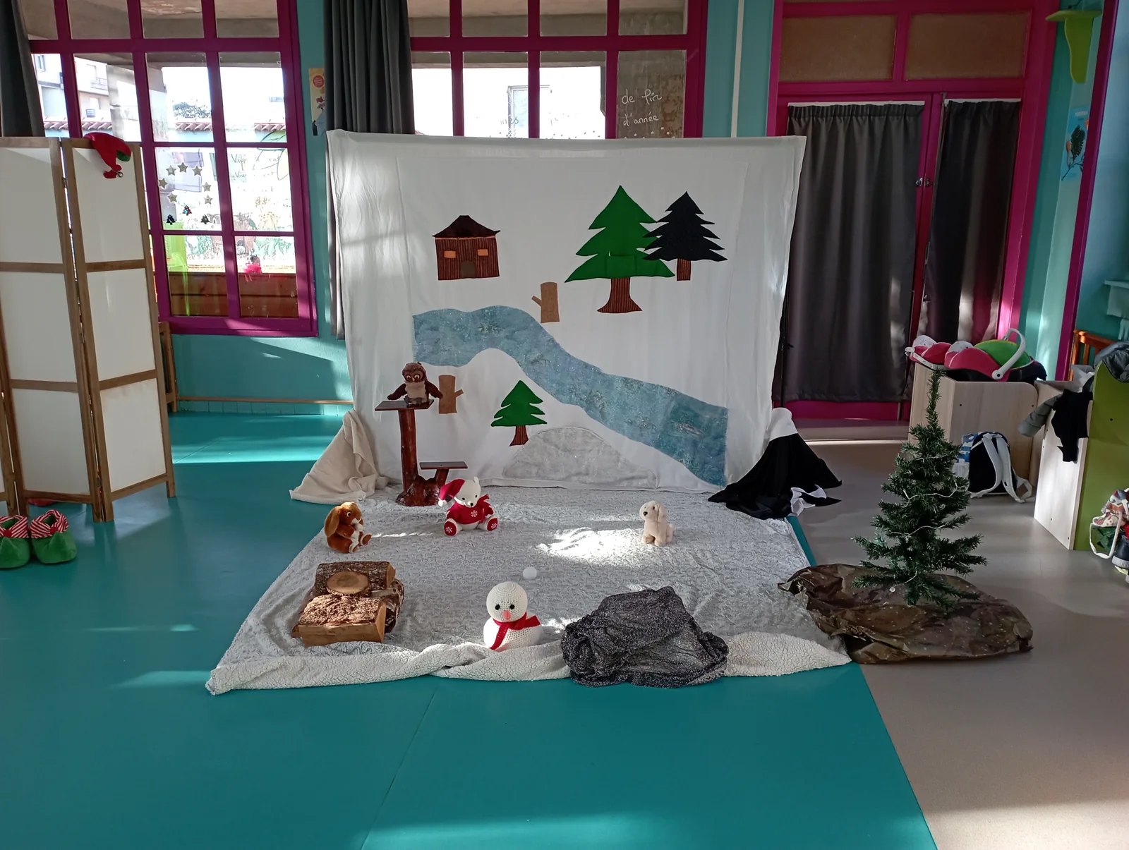 Le décor du Ruban de Noël : un grand support vertical en tissu avec la forêt enneigée, la rivière, les sapins et le chalet