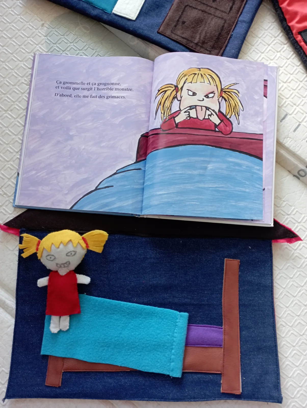 Un livre en tissu ouvert à côté de l'album qu'il reprend : une fillette dans son lit, cousue en feutrine