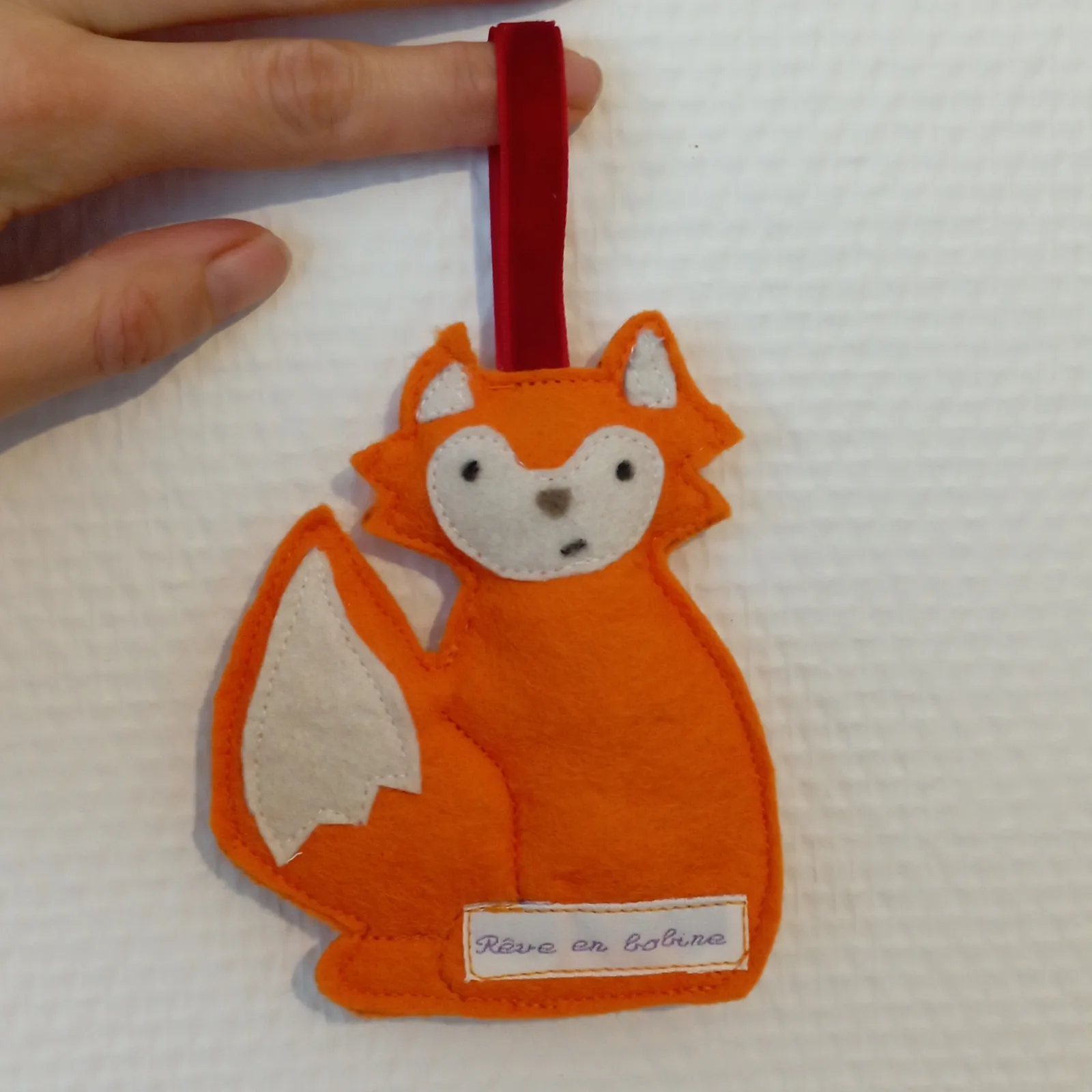 Un petit renard en feutrine orange, avec une étiquette Rêve en Bobine