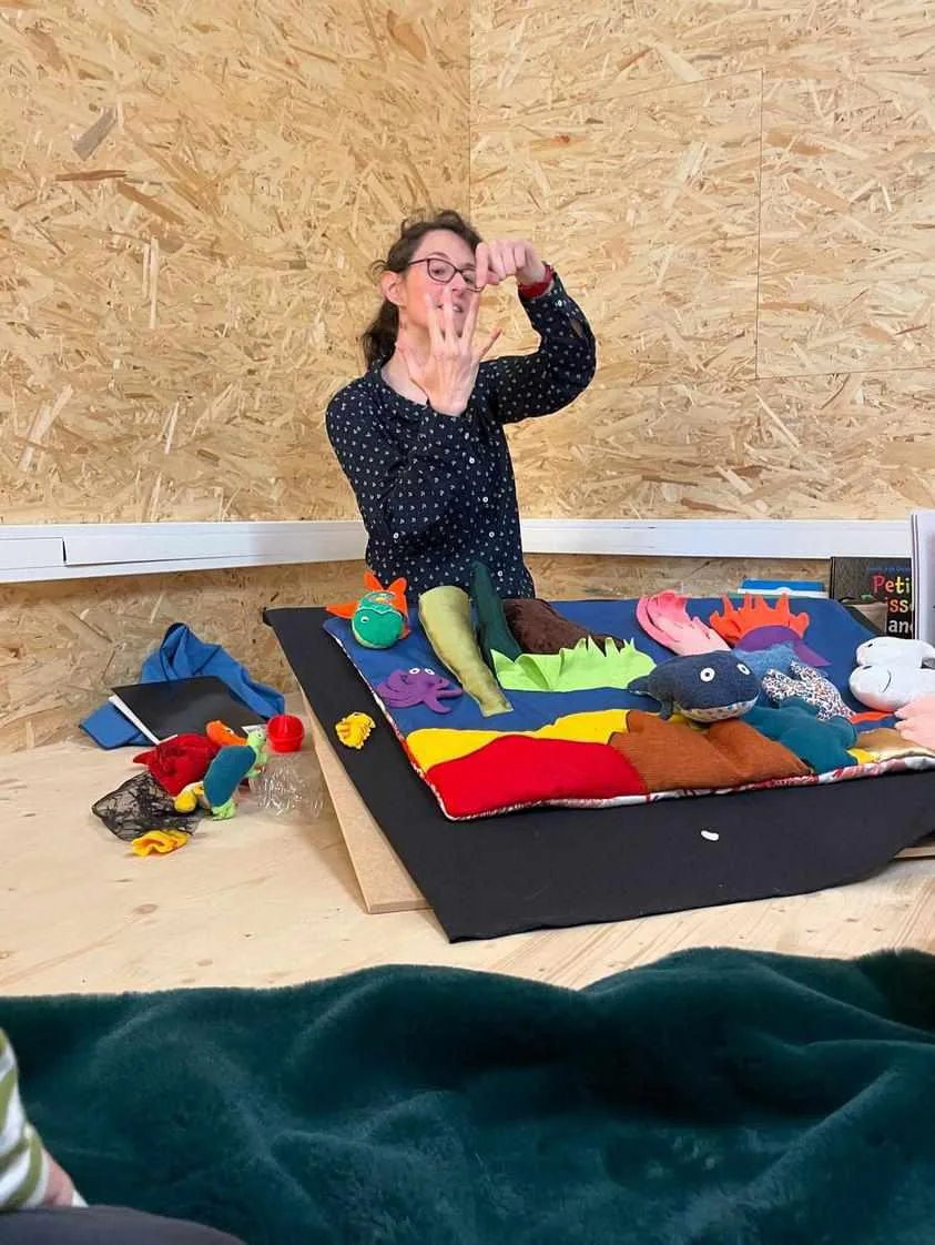 Laetitia fait surgir un personnage en tissu au-dessus du tapis de lecture, devant les enfants